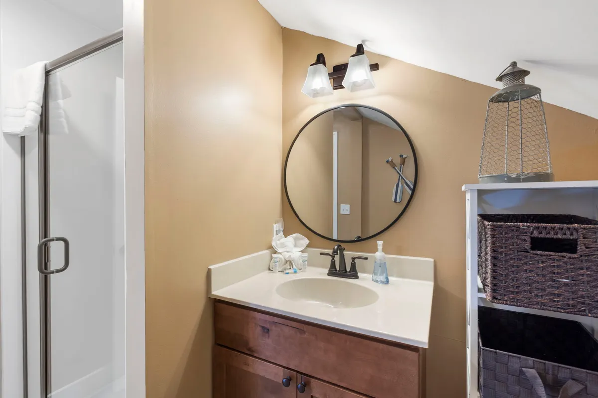 The image spotlights a vanity area with a sink, round mirror, light fixtures, and a storage shelf. The calming mood and practical features suggest a private half-bath space, supporting convenience and comfort for loft guests.