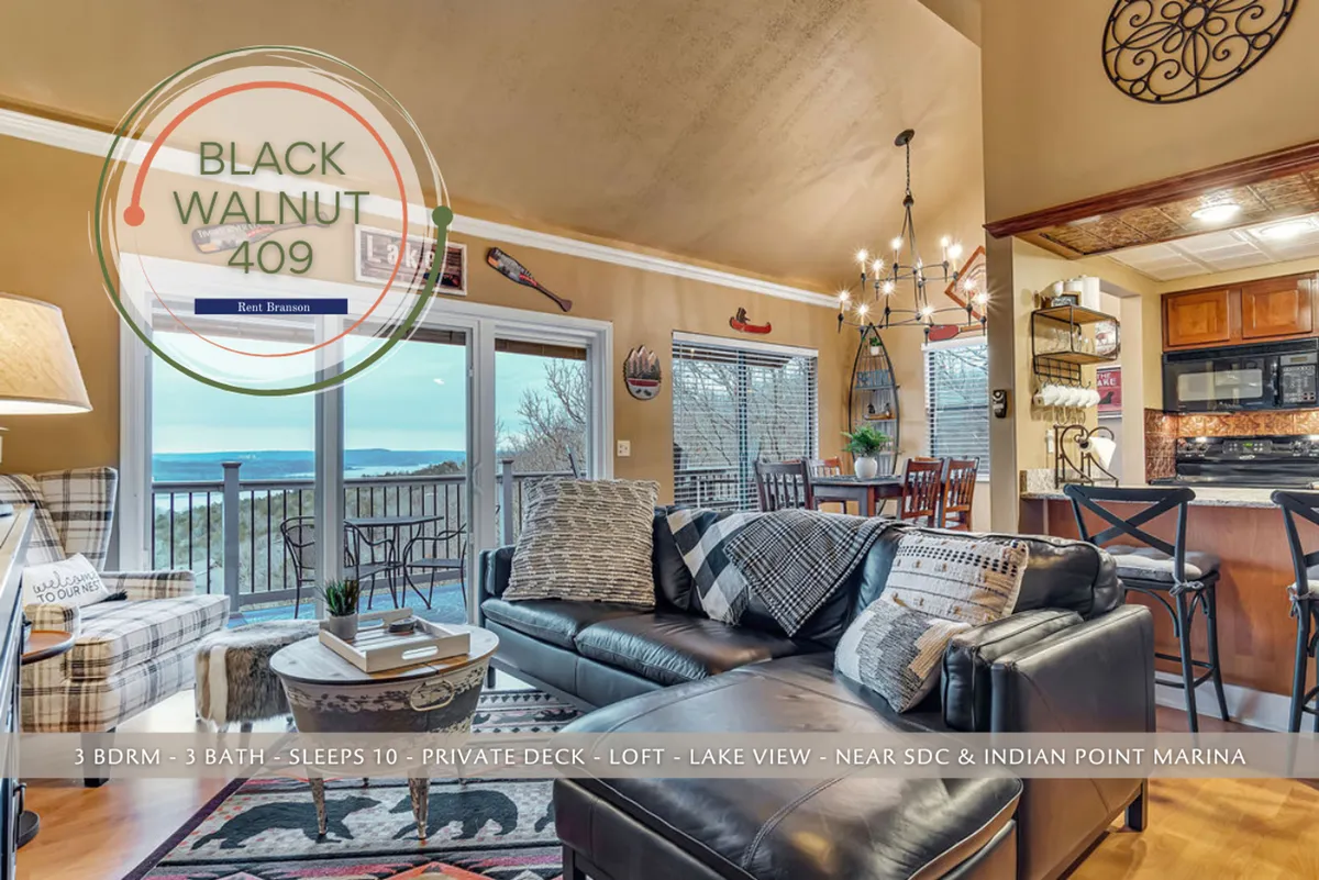 A cozy, welcoming living area with a comfortable leather sofa, large windows that perfectly frame the lake, decorative wall art, and a visible kitchen area in the background. The layout demonstrates the open plan and the way natural light and views are integrated into daily life.