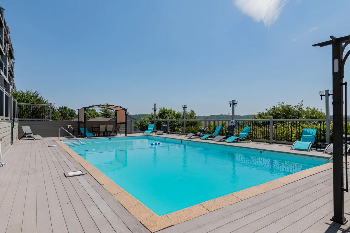 A sun-drenched outdoor swimming pool area featuring lounge chairs and a shaded canopy. The pool is surrounded by a relaxing patio, making it perfect for family fun and social gatherings in the summer months.