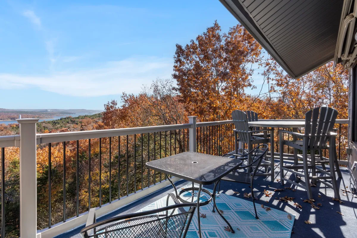 A serene private deck with comfortable outdoor seating, surrounded by fall foliage and set against a scenic view of the lake and valley. The space evokes morning coffees and sunset celebrations, blending indoor comfort with outdoor beauty.