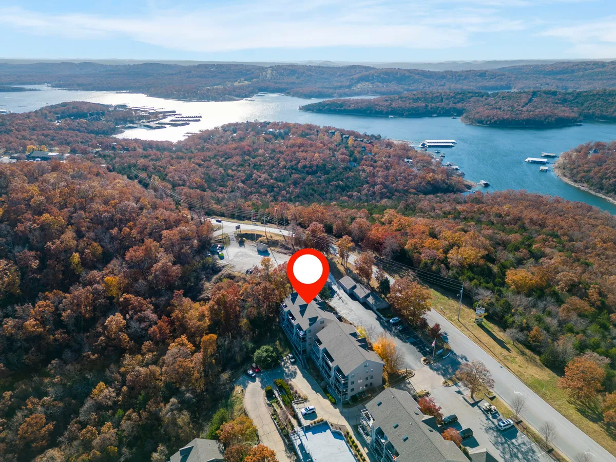 A serene view of Table Rock Lake surrounded by vibrant autumn foliage, with buildings and a road visible along the shoreline. The water is calm, inviting, and the natural landscape dominates the scene.