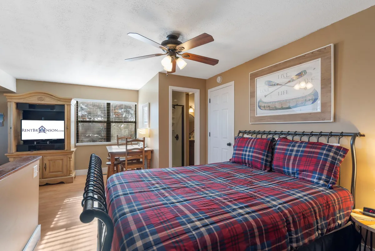 A welcoming bedroom with a plaid bedspread, wooden furniture, a television, and a desk with a chair, providing both relaxation and entertainment options.