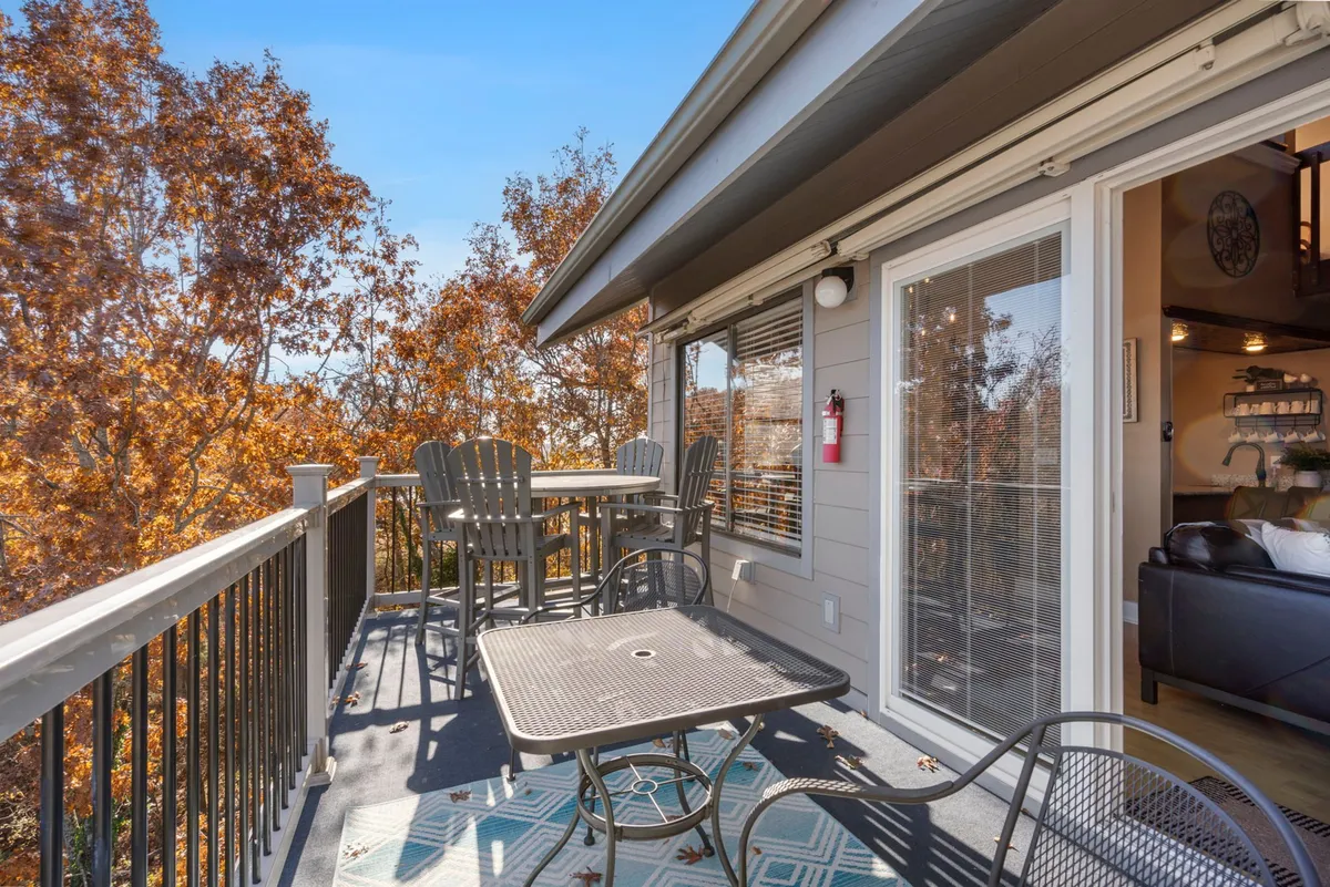 A peaceful outdoor dining area on a deck or patio, with a table and chairs overlooking colorful autumn trees. The setting evokes quiet mornings and relaxed evenings immersed in nature.