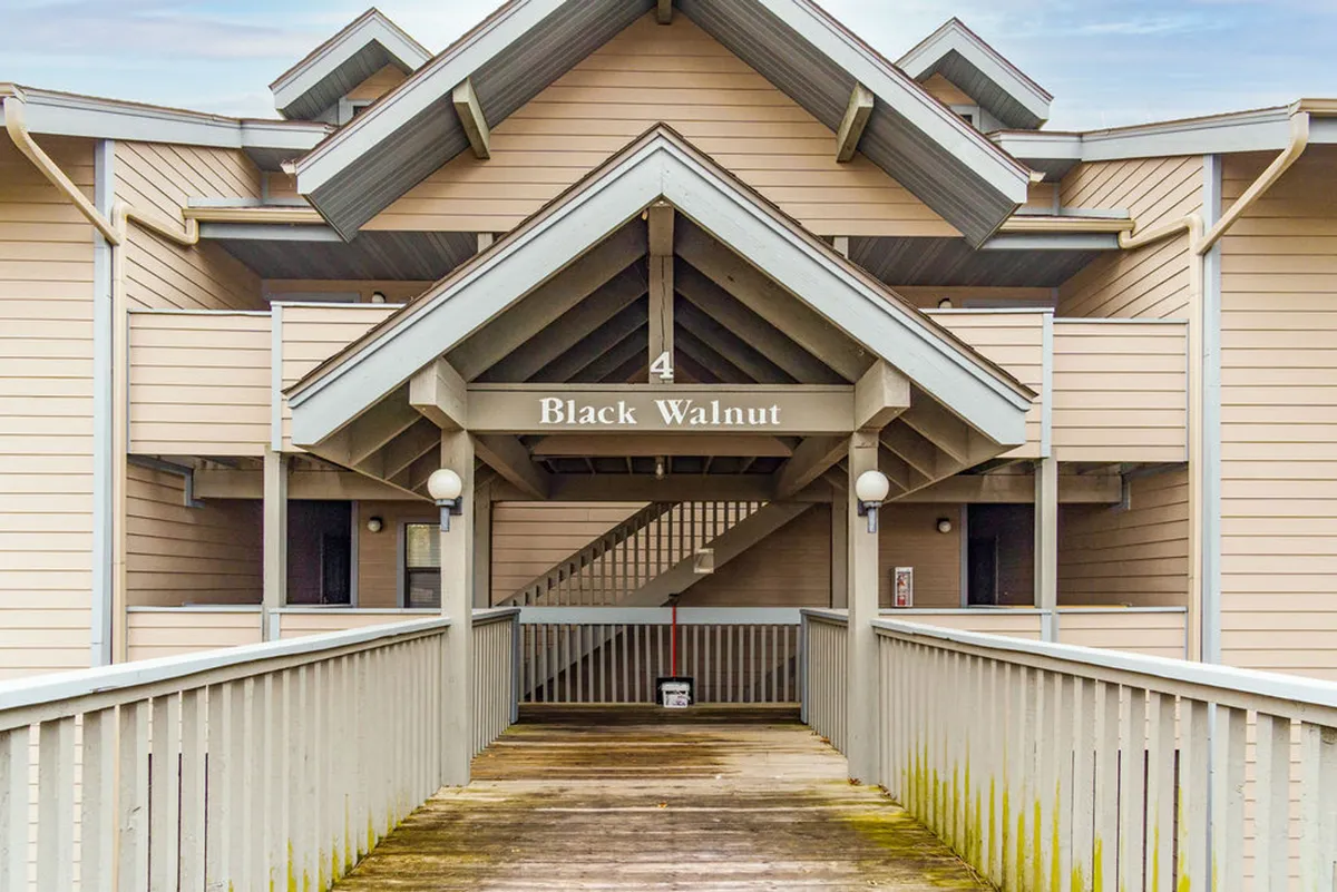 This image features the exterior entrance of the condo building, highlighting the inviting archway, staircase leading up to the top-floor unit, railings, and a prominent 'Black Walnut' name sign. The scene gives a clear sense of arrival and the multi-level, stair-accessible nature of the property.
