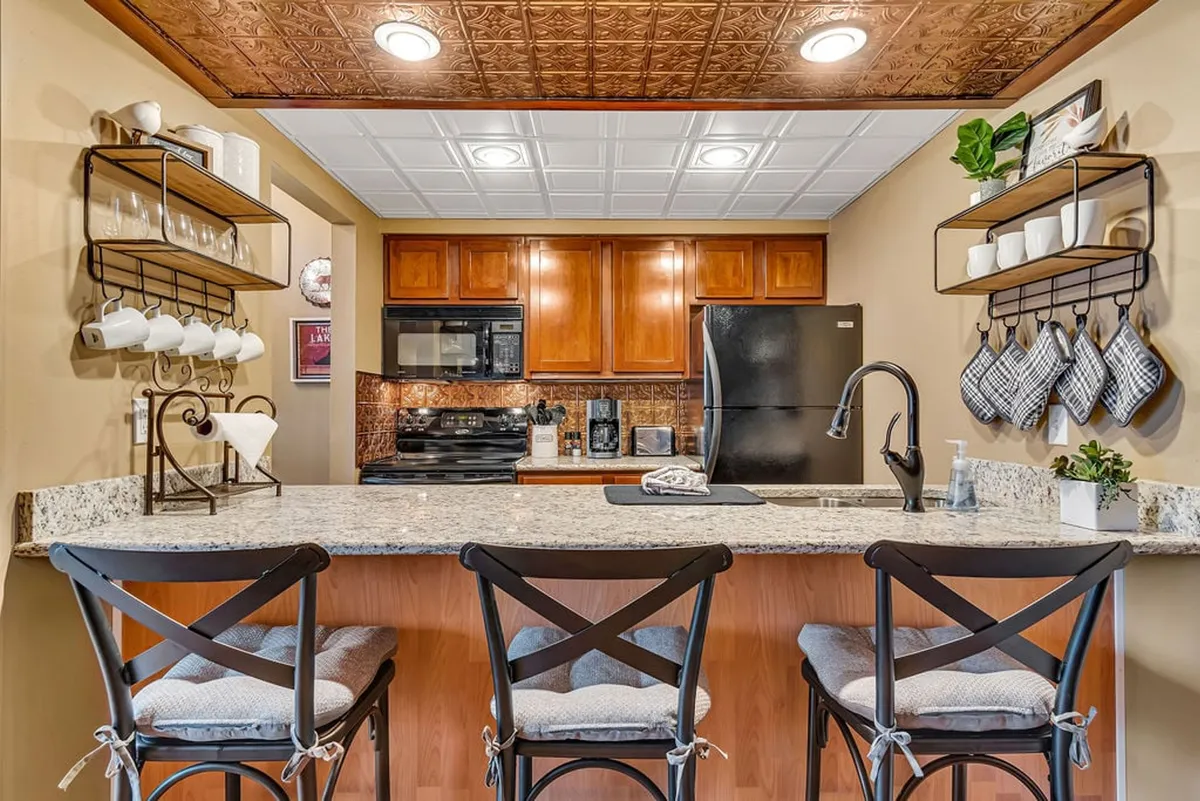 A warm, inviting kitchen featuring a granite countertop, wooden cabinets, updated black appliances, a decorative dish rack, and hanging towels. The kitchen is designed for both practicality and style, inviting shared cooking and dining experiences.