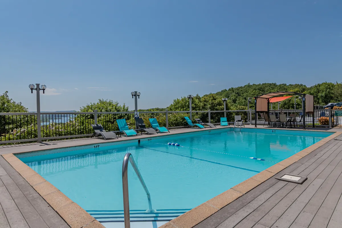 An inviting outdoor community pool area with swim-ready water, lounge chairs, a cabana, and a backdrop of scenic natural landscape. The mood is leisurely and cheerful, perfect for relaxation or socializing in a resort-like setting.