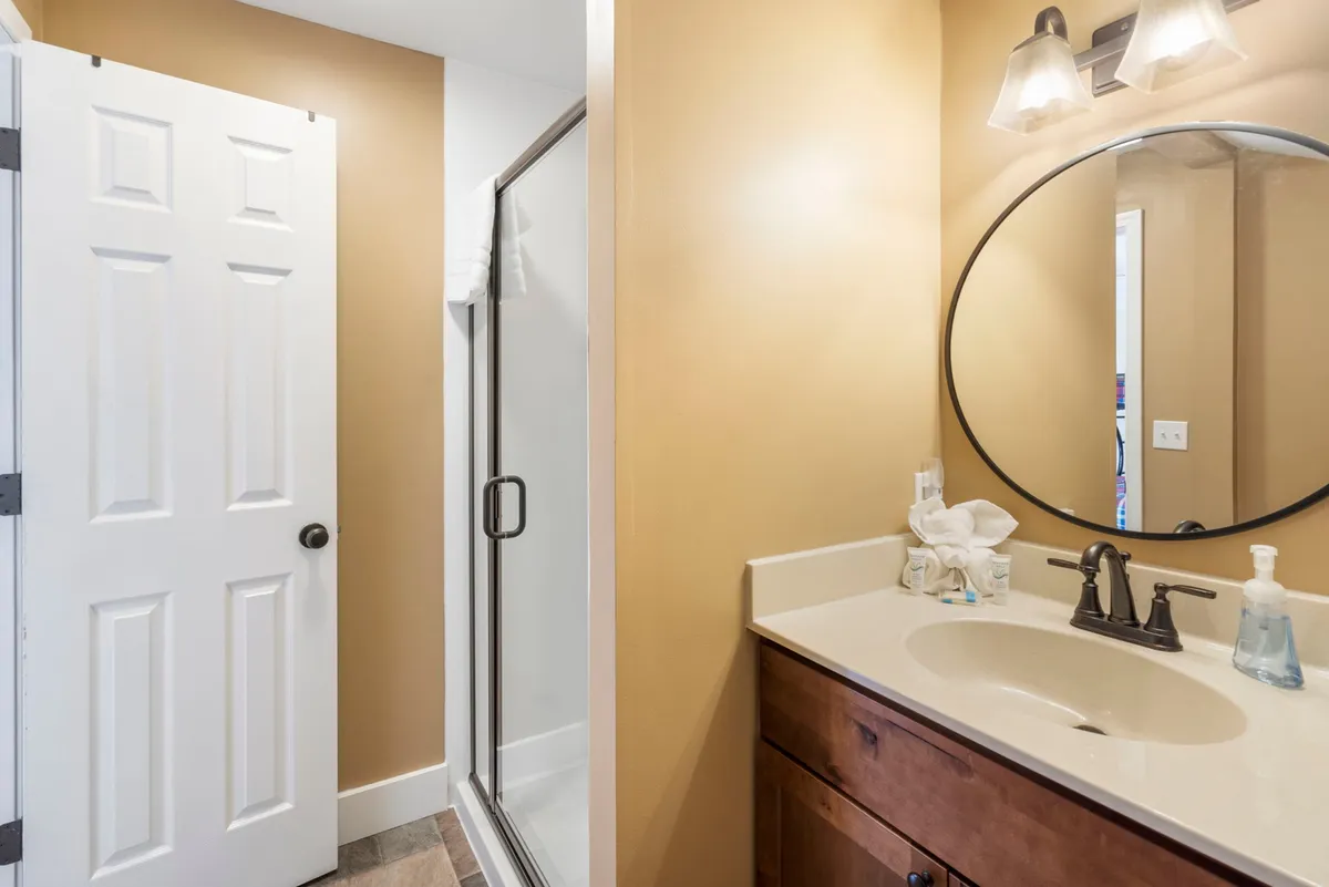 A modern bathroom interior featuring a vanity with a sink and mirror, a shower enclosure, and a door—offering a calm and inviting space for personal routines.