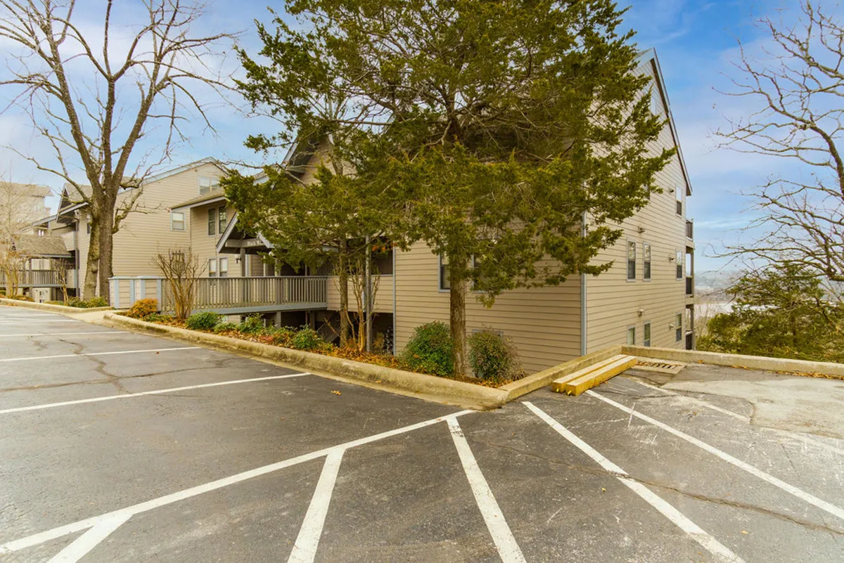 This exterior shot showcases the overall building structure surrounded by lush greenery and a convenient parking area, conveying a sense of the property's peaceful location and easy arrival for guests. The landscape gives context to the home's setting within the broader neighborhood.